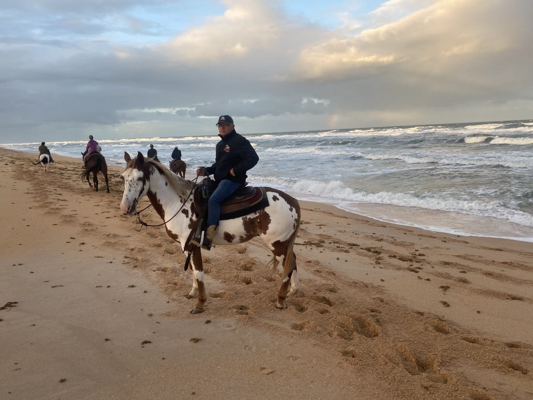 A guided group riding horses along the surf line of a Florida beach under a big sky